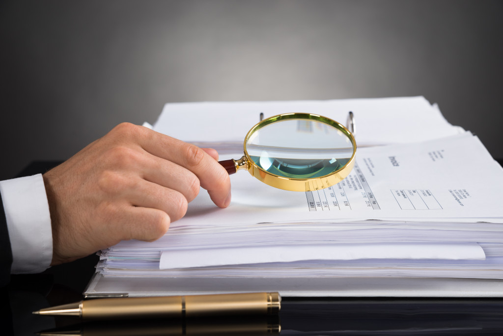 businessman holding magnifying glass on top of business documents