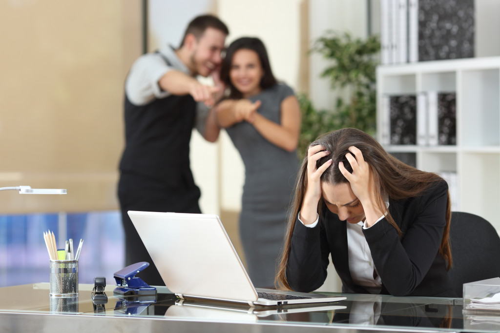 Coworkers laughing at a distraught woman in the office