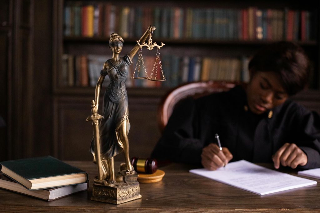 judge signing a document at a desk, with a Lady Justice figurine beside her